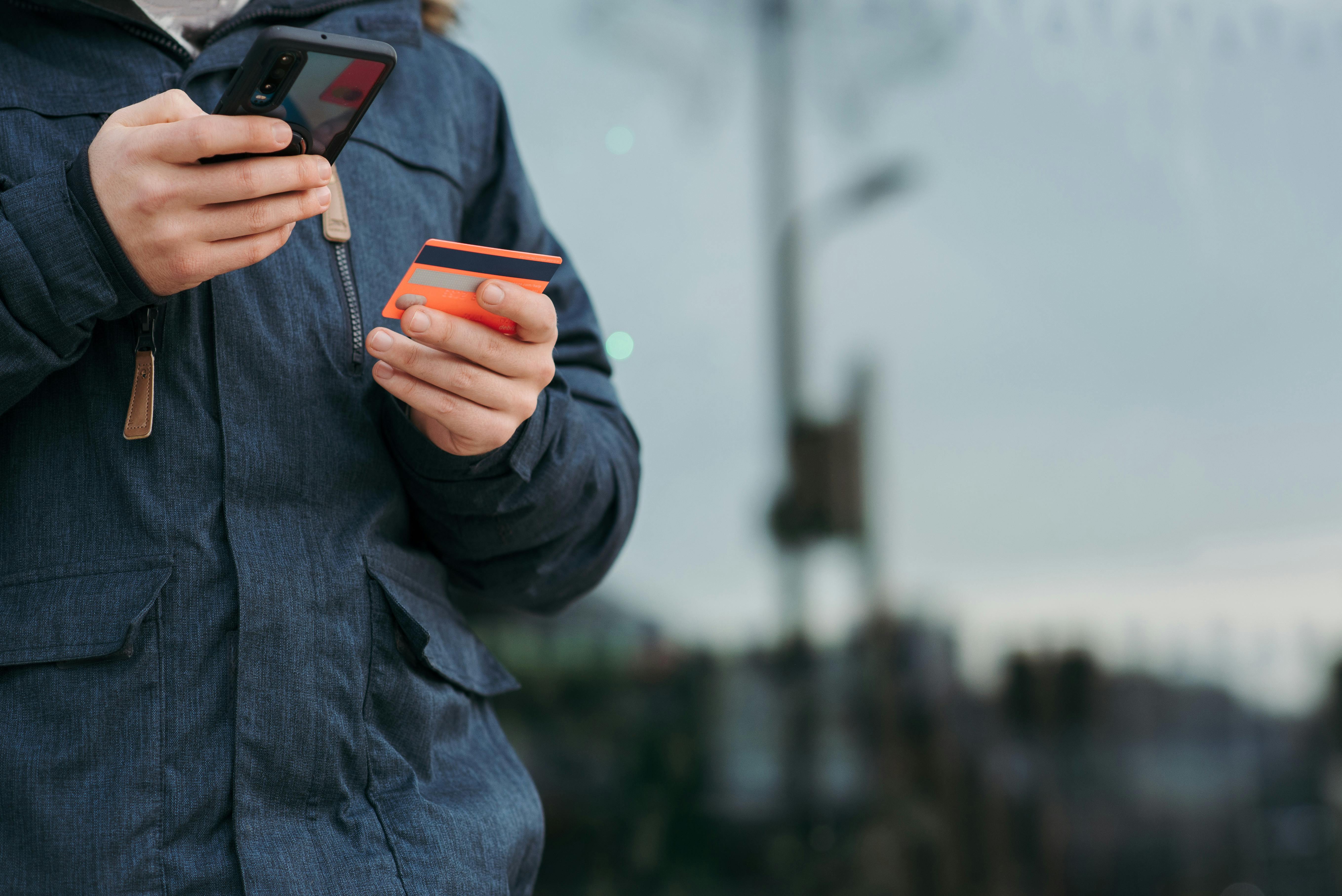 A person outdoors using a smartphone and credit card, illustrating online payments.